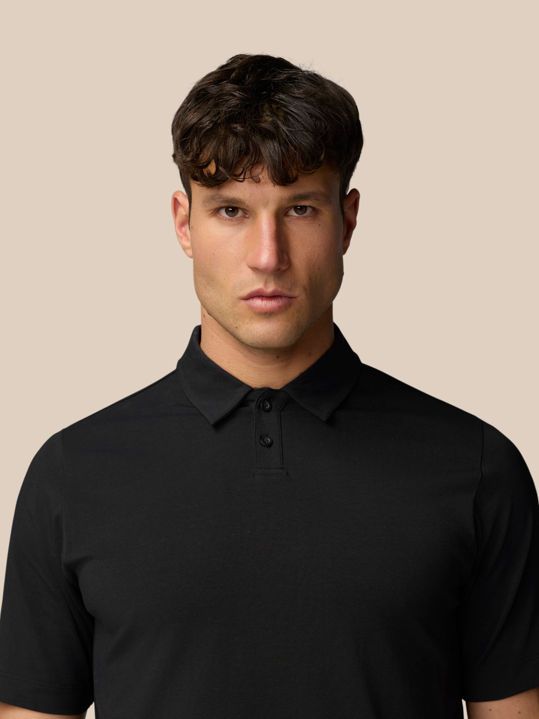 Male model in black Travel Polo facing forward against a beige background