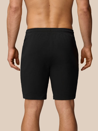 Back view of a man wearing black travel shorts with an elastic waistband against a beige background.