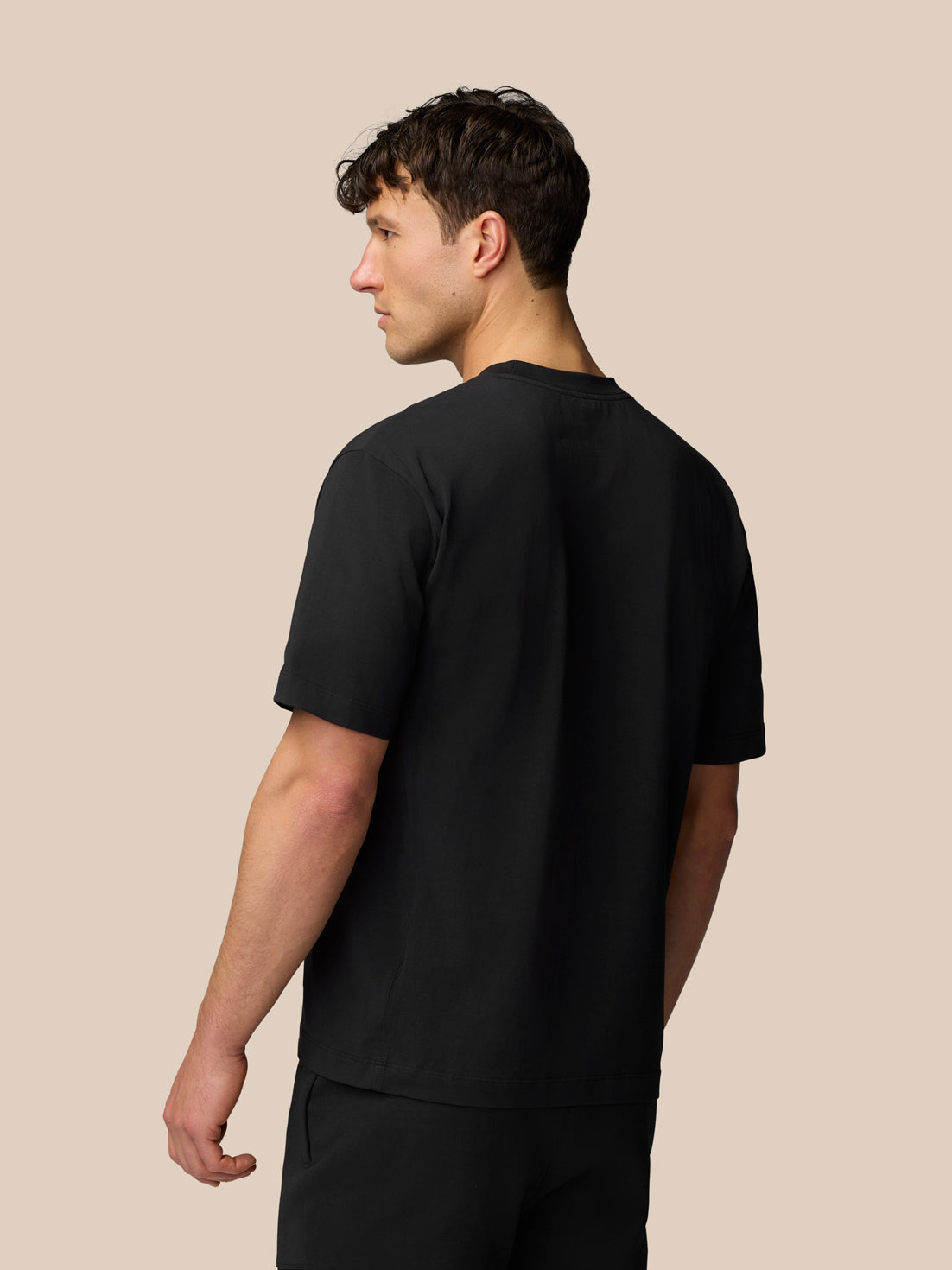 Back view of a man wearing a black Travel T Shirt with short sleeves and relaxed fit