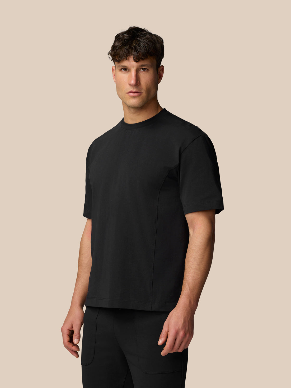 Three-quarter view of a man wearing a black Travel T Shirt against a beige background