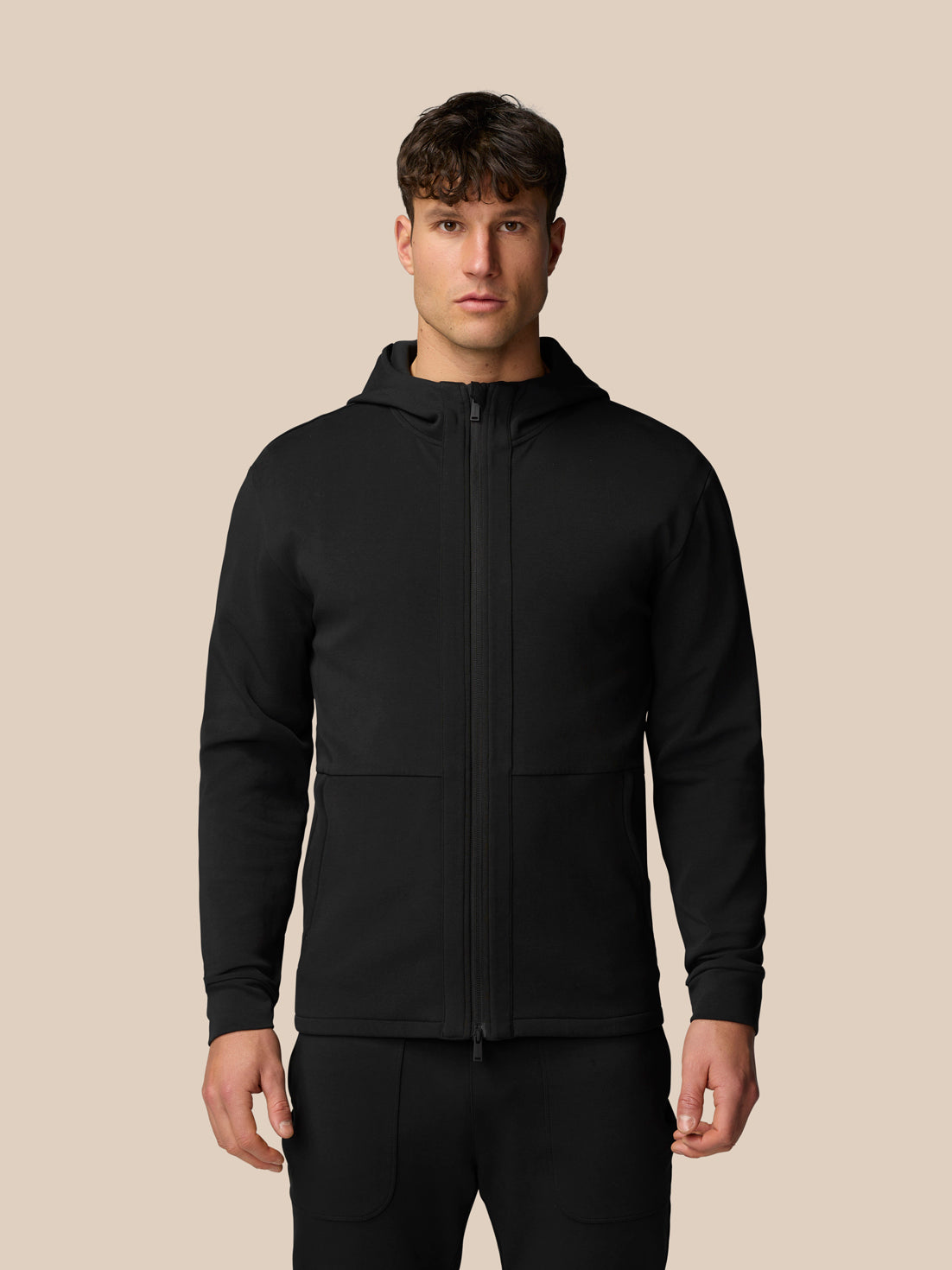 Front view of a man wearing a black travel full zip hoodie with a hood and a centered zipper.