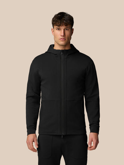 Front view of a man wearing a black travel full zip hoodie with a hood and a centered zipper.