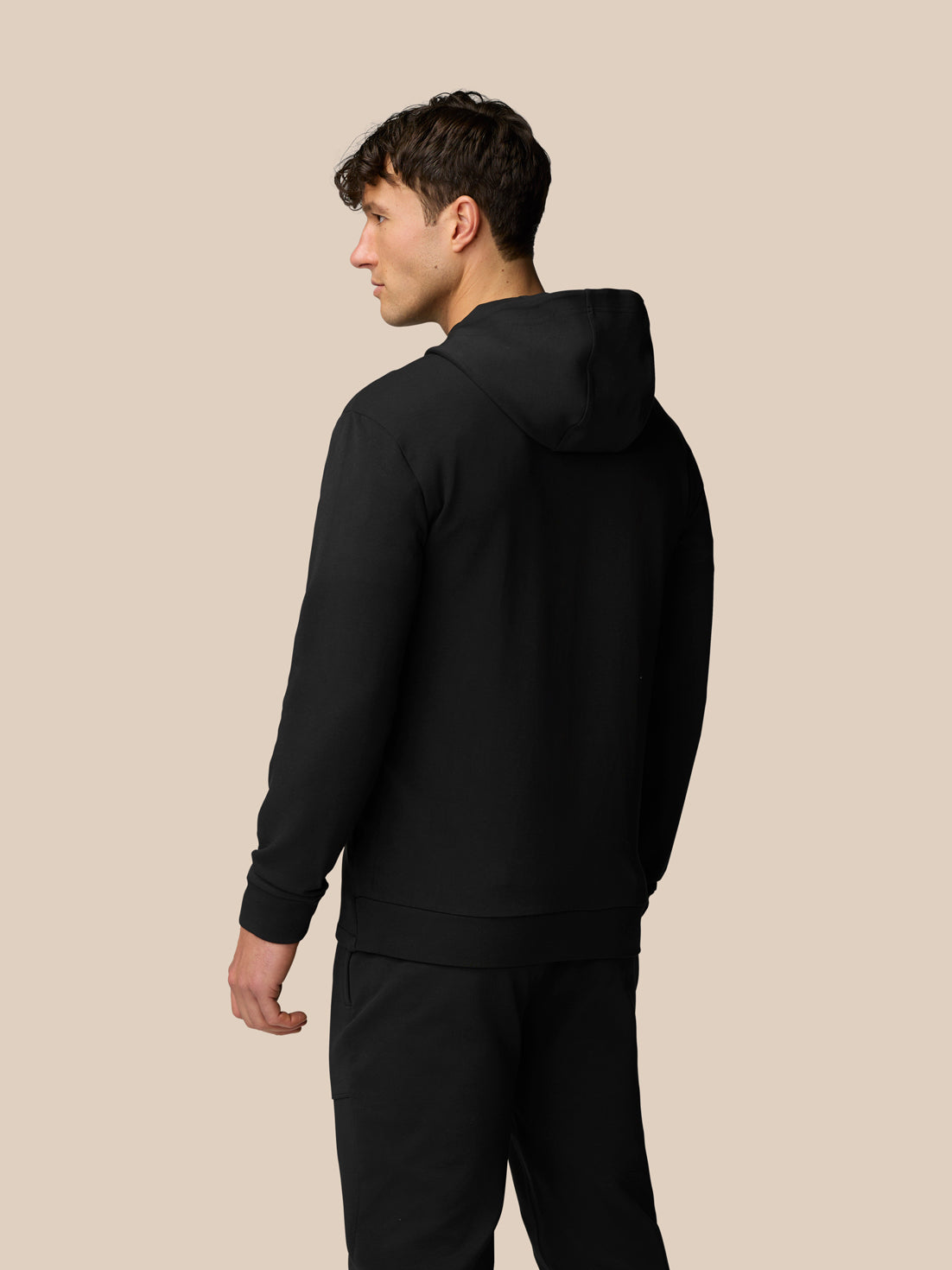 Back view of a man wearing a black Travel Full Zip Hoodie with hood down and clean lines