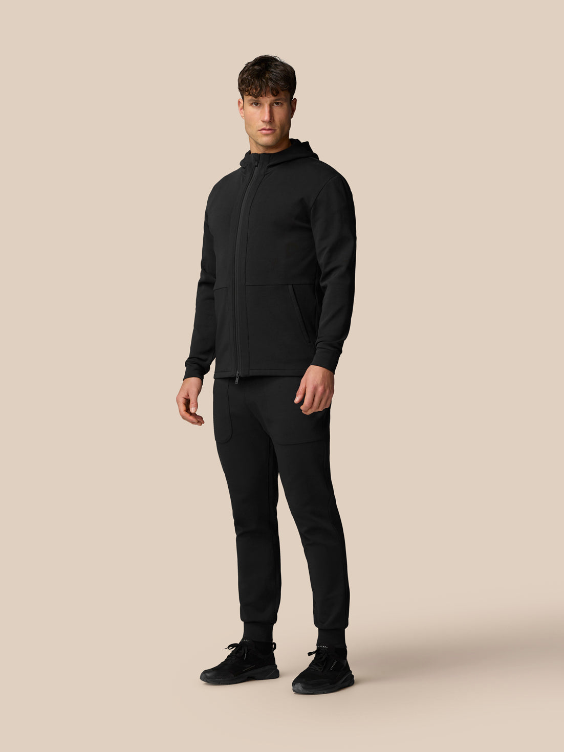 Full-body shot of a man in black travel full zip hoodie with matching pants.