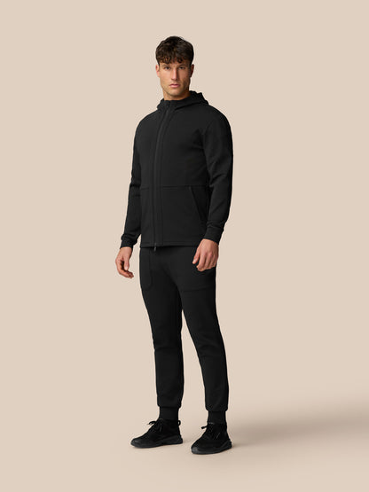 Full-body shot of a man in black travel full zip hoodie with matching pants.
