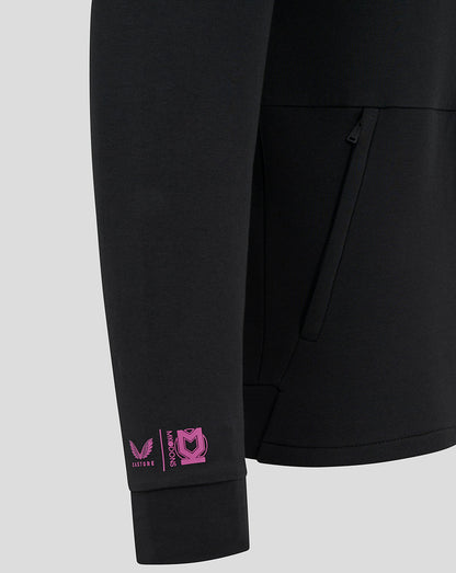 Close-up of black jacket sleeve with pink Castore and MK Dons logos near the cuff