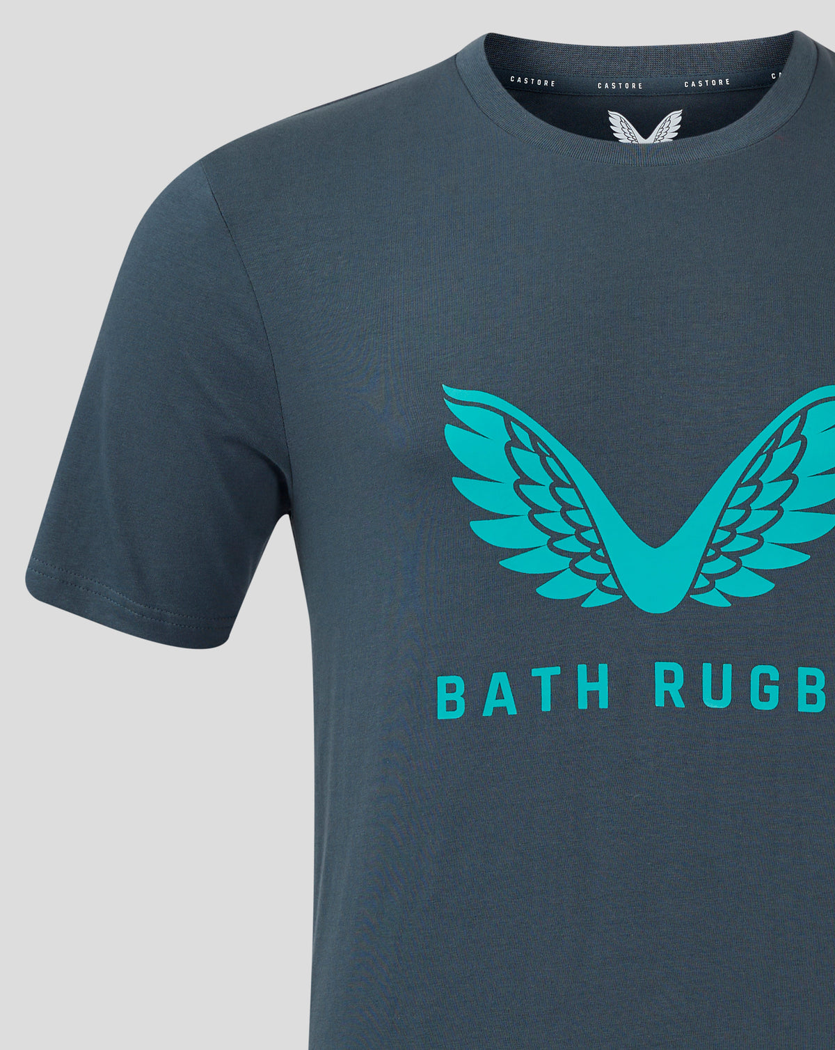 Close up of Bath Rugby T shirt chest with turquoise wing emblem on dark slate fabric and a visible crew neck.