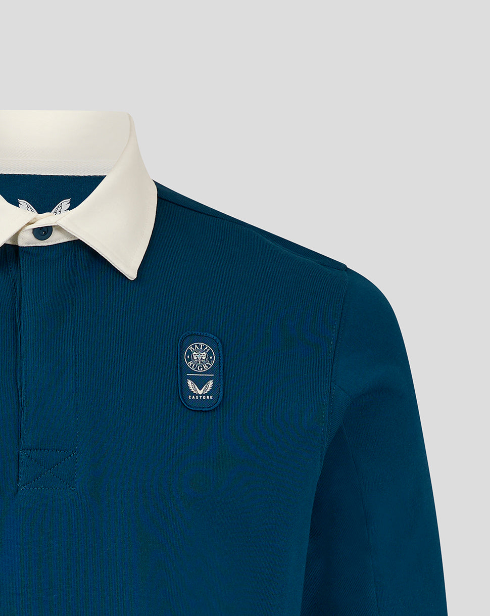 Close-up of teal Bath Rugby Junior Jersey Top showing white collar and a badge patch with Bath Rugby crest and Castore logo on the chest.