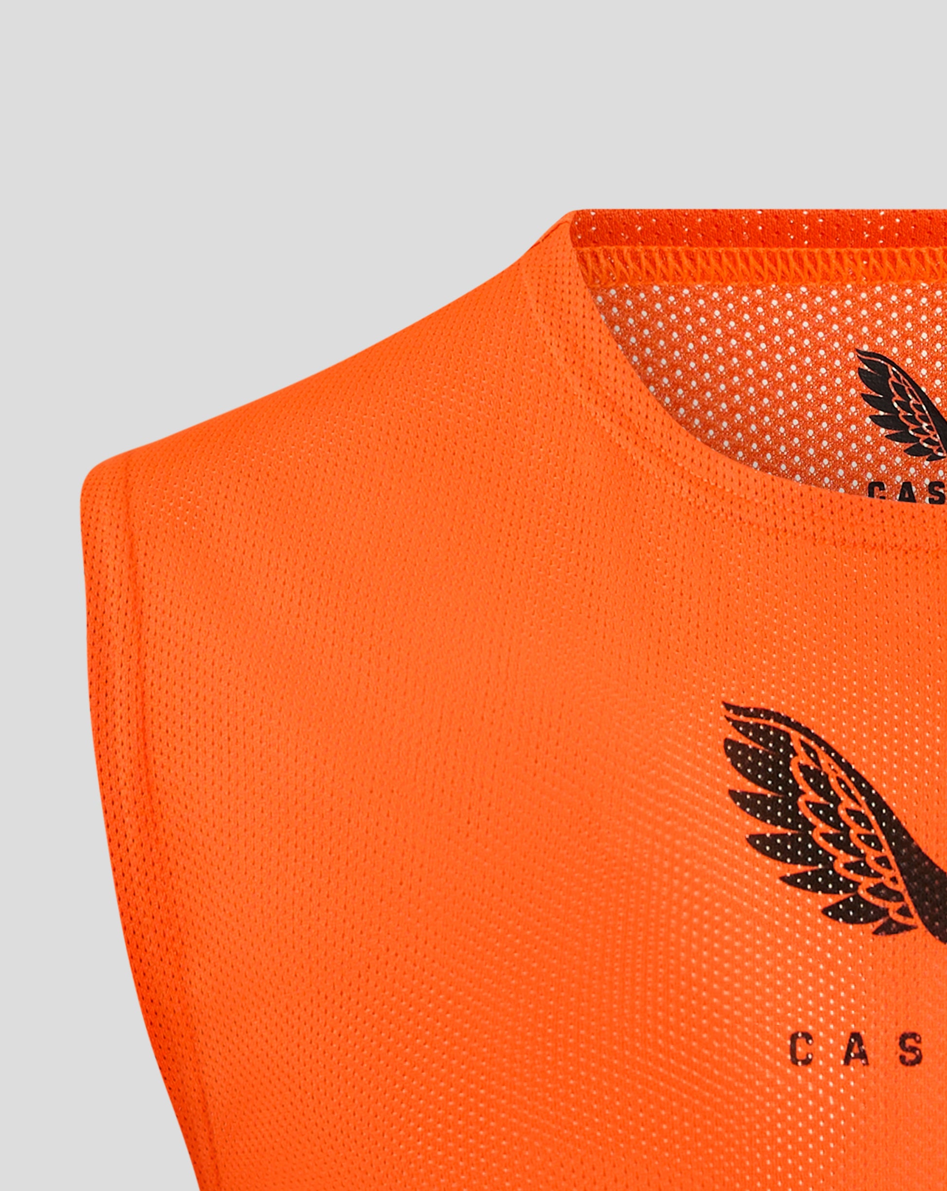 Bright orange junior training bib fabric close-up with perforated mesh and partial Castore logo