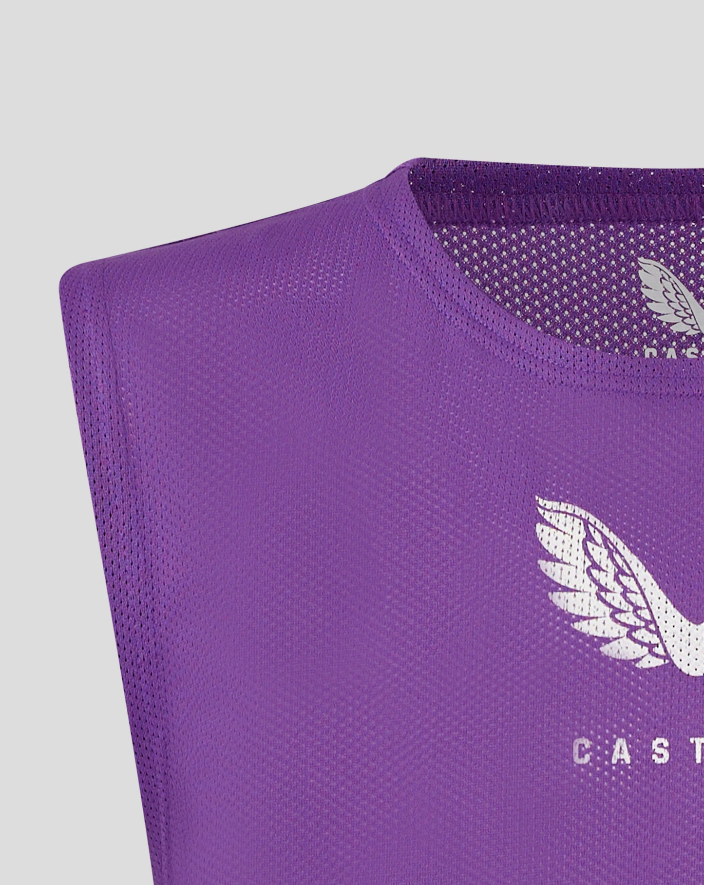 Close up of a purple junior training bib fabric showing a scoop neckline, mesh texture, and a white Castore logo.