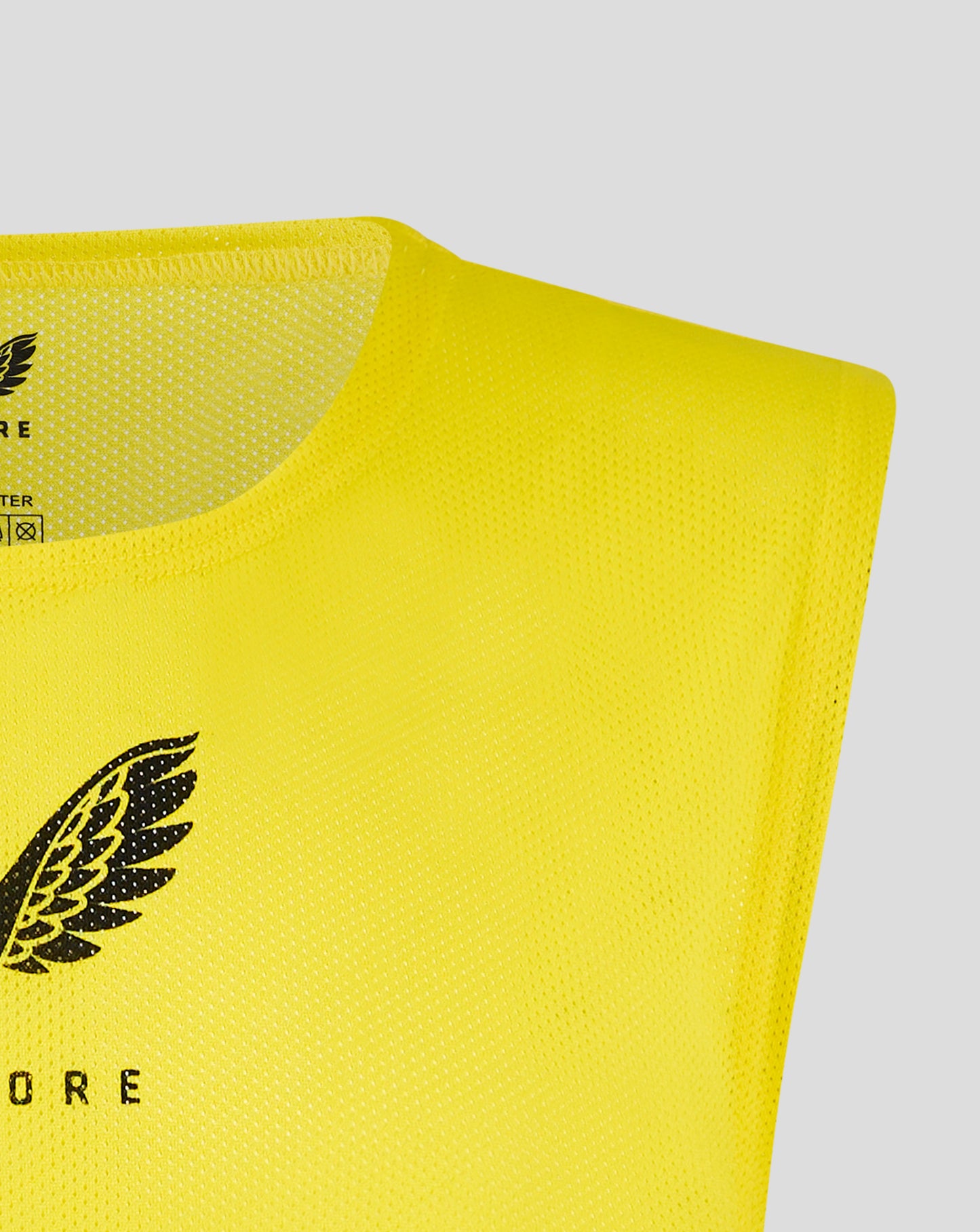 Close-up of bottom left area of bright yellow junior training bib with a black Castore wing emblem