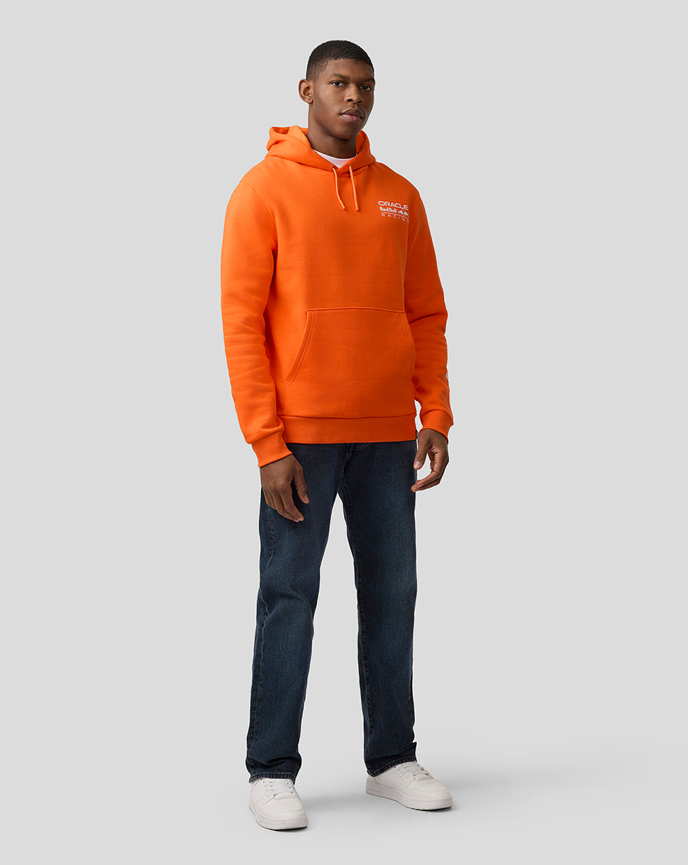 Full-body shot of a man in an orange Oracle Red Bull Racing hoodie with chest logo and white sneakers