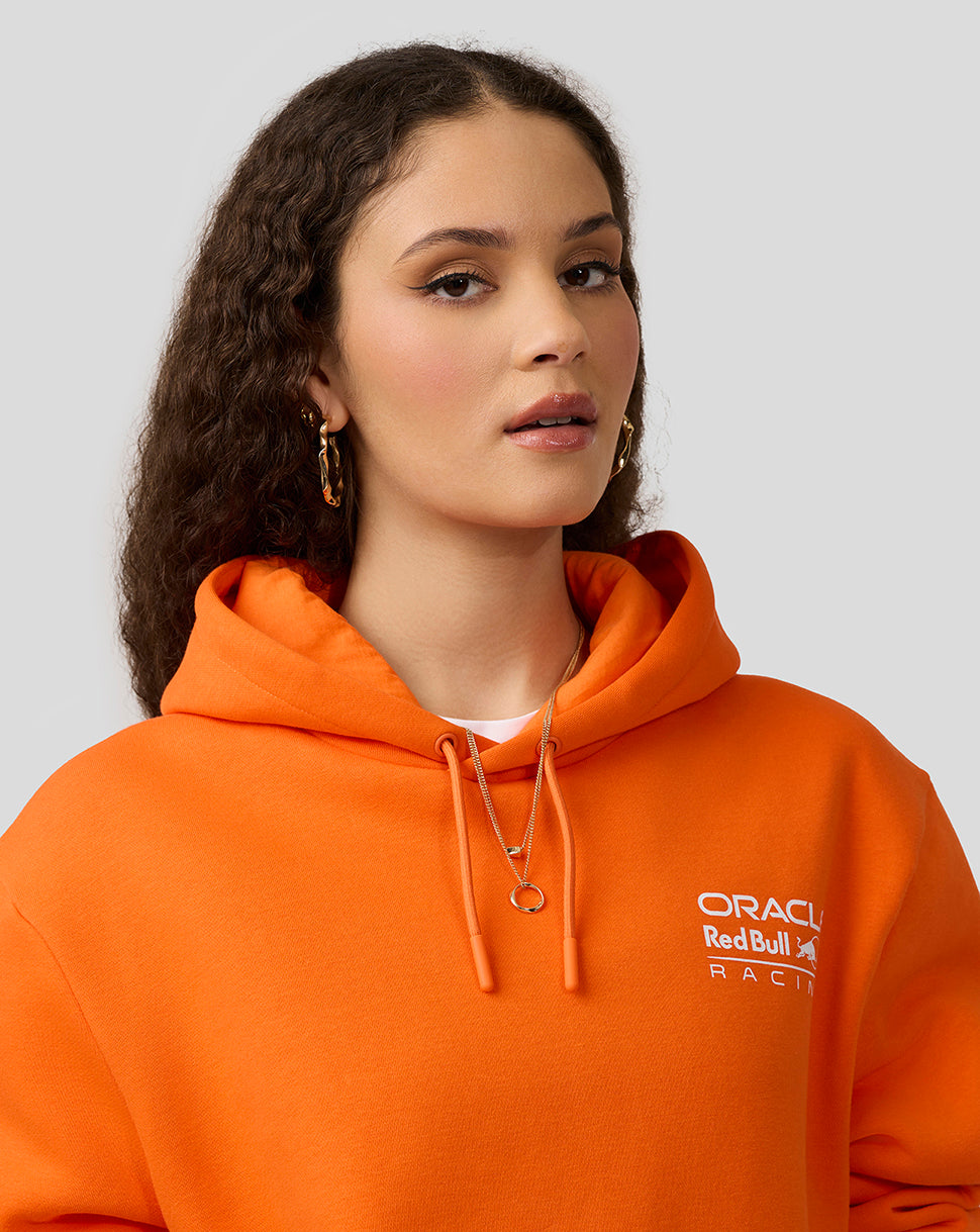 Close-up of a woman wearing an orange Oracle Red Bull Racing hoodie with chest logo and drawstring hood
