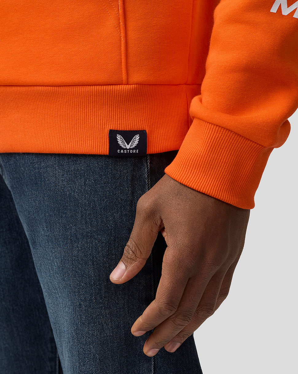 Close-up of orange hoodie pocket and ribbed hem with Castore label and a resting hand in the pocket.