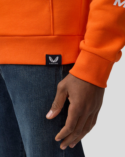 Close-up of orange hoodie pocket and ribbed hem with Castore label and a resting hand in the pocket.
