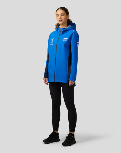 Female model in lapis blue BWT Alpine water resistant jacket with hood and front zip, featuring sponsor logos on chest