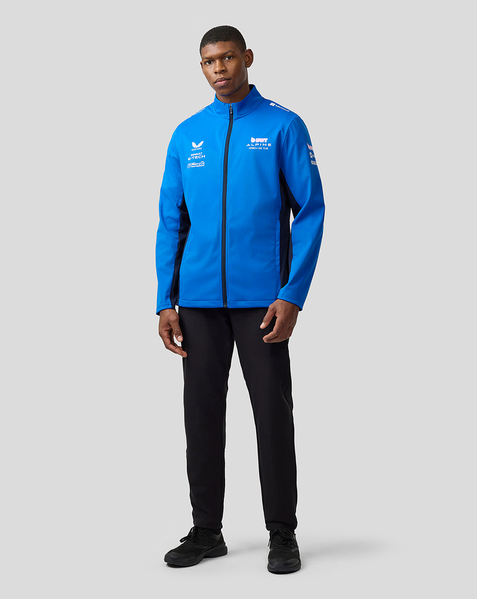Full-body shot of a man wearing a lapis blue BWT Alpine soft shell jacket with black pants.