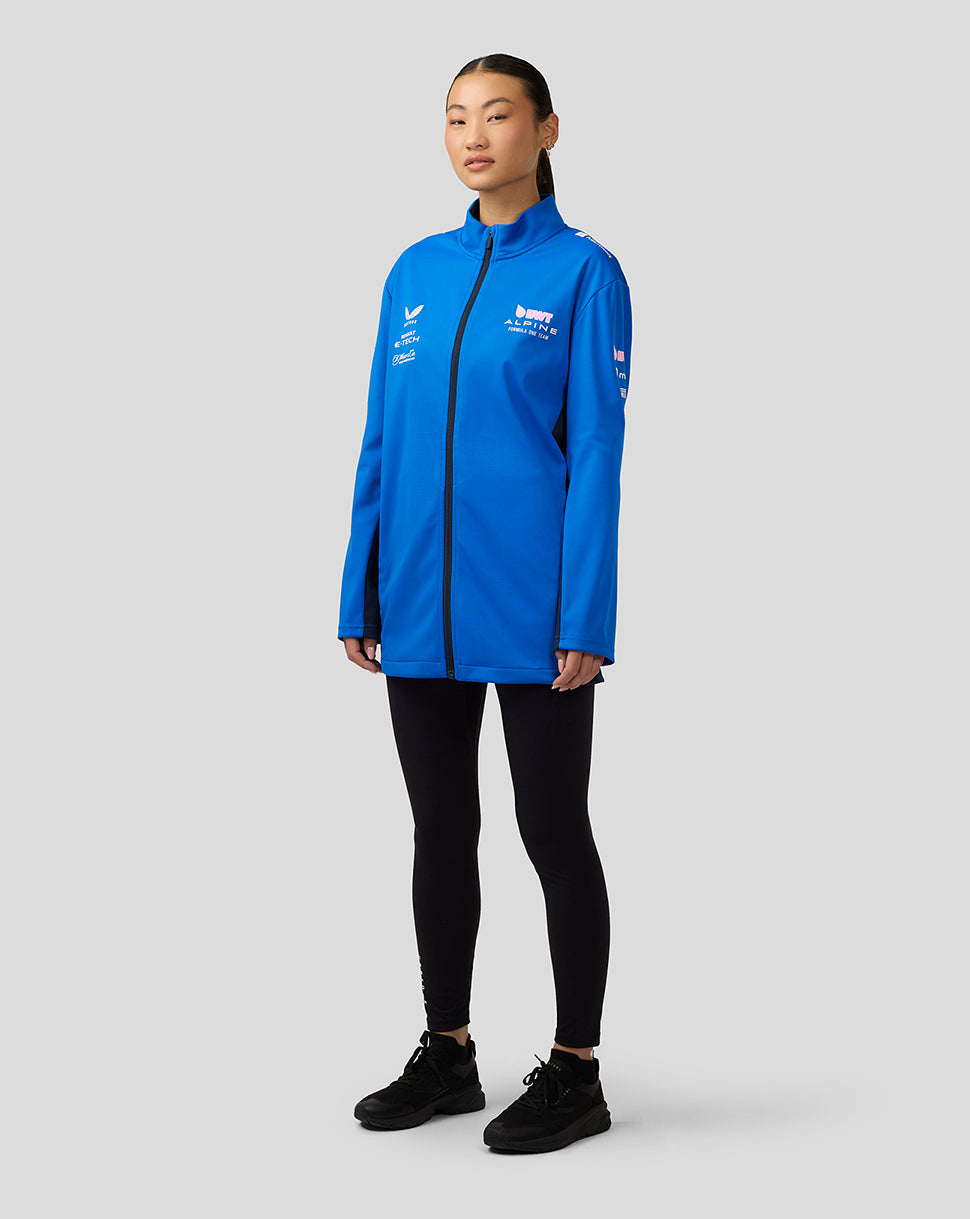 Woman wearing lapis blue BWT Alpine Formula One Team unisex soft shell jacket with funnel neck and front zip.