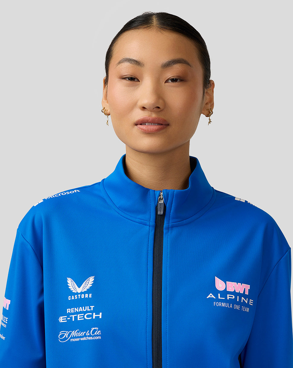 Portrait of a model in a lapis blue BWT Alpine soft shell jacket with zipper and sponsor logos.