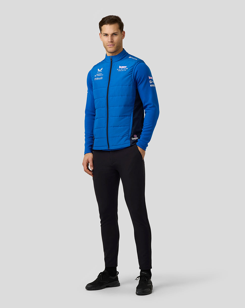Full body view of a male model wearing the lapis blue BWT Alpine Formula One Team hybrid gilet over a blue top and black pants