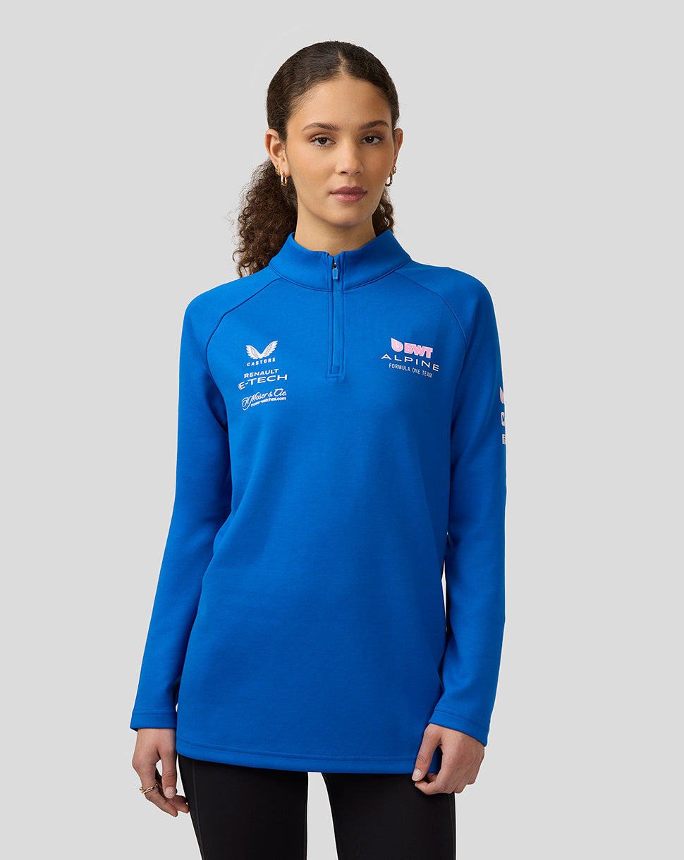 Front view of a woman wearing lapis blue BWT Alpine quarter zip midlayer with chest and sleeve logos.