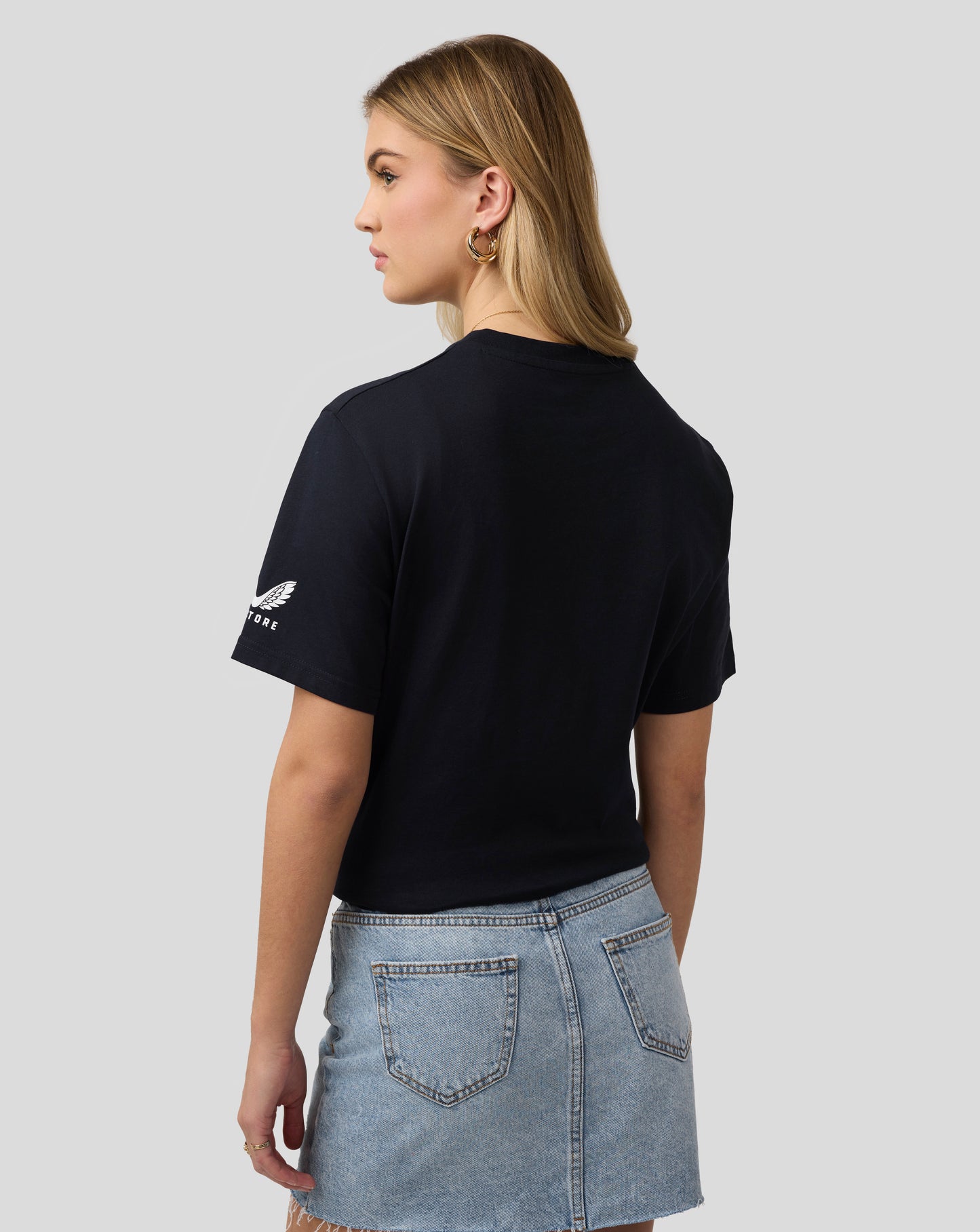 Back view of a woman wearing a navy Castore T shirt with white wing logo on the sleeve