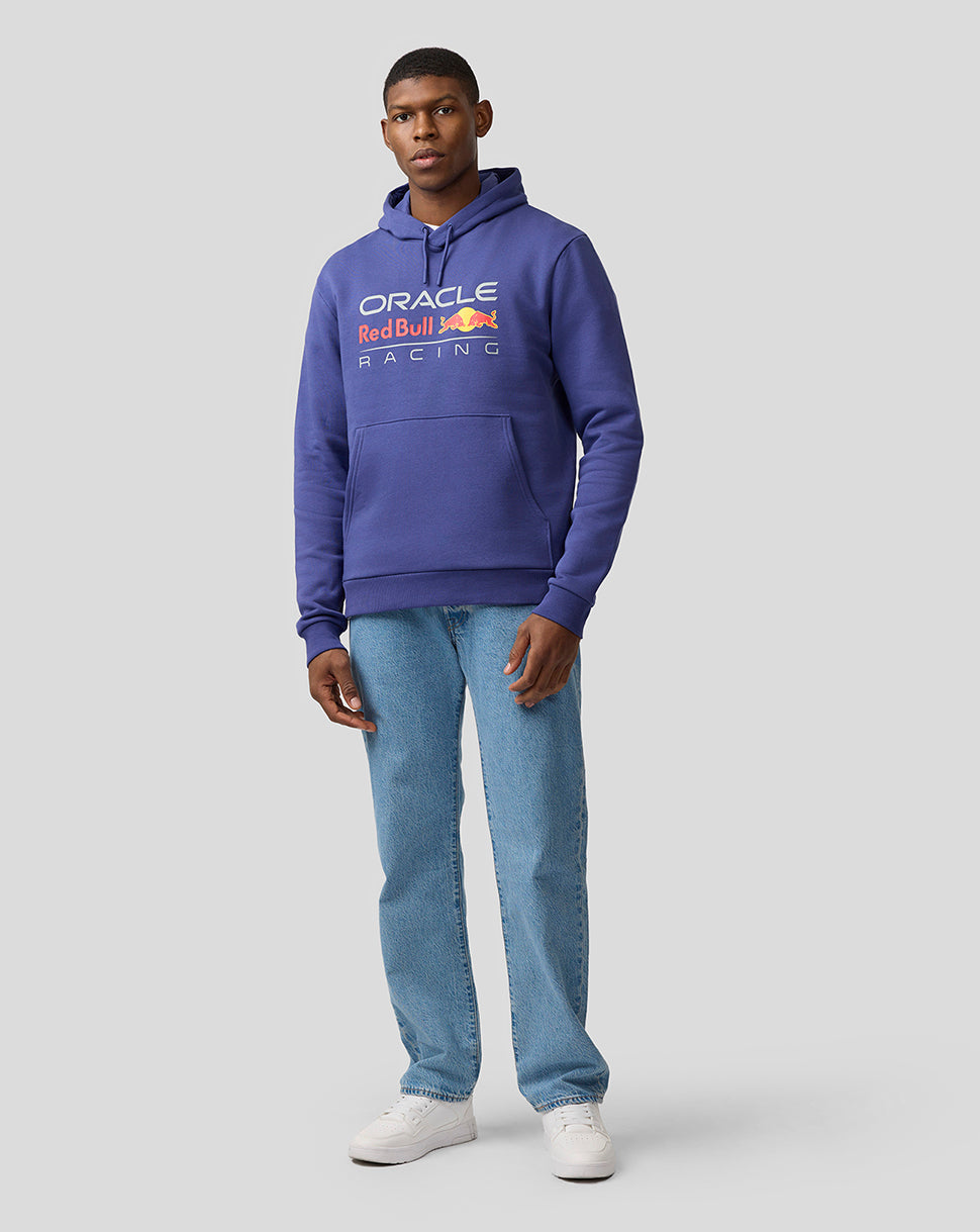 Male model in Skipper Blue Oracle Red Bull Racing hoodie posing with hands in pockets and white sneakers.