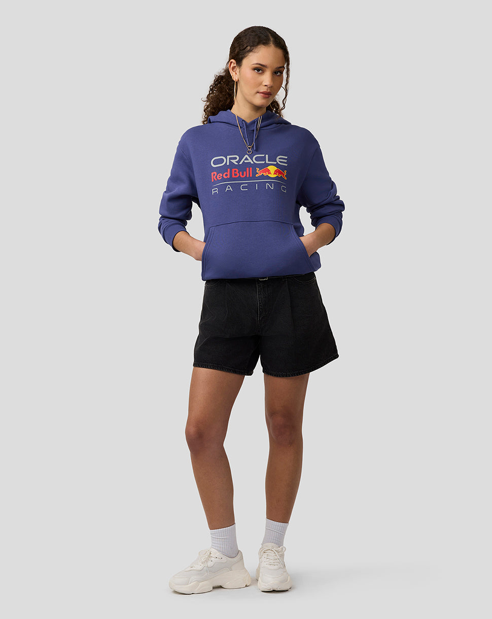 Female model wearing Skipper Blue Oracle Red Bull Racing hoodie with hands in pockets and large front logo.