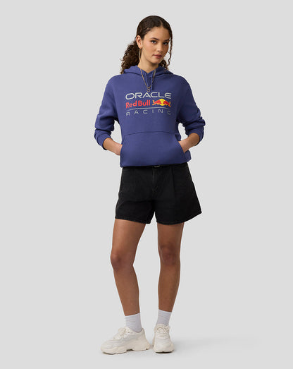 Female model wearing Skipper Blue Oracle Red Bull Racing hoodie with hands in pockets and large front logo.