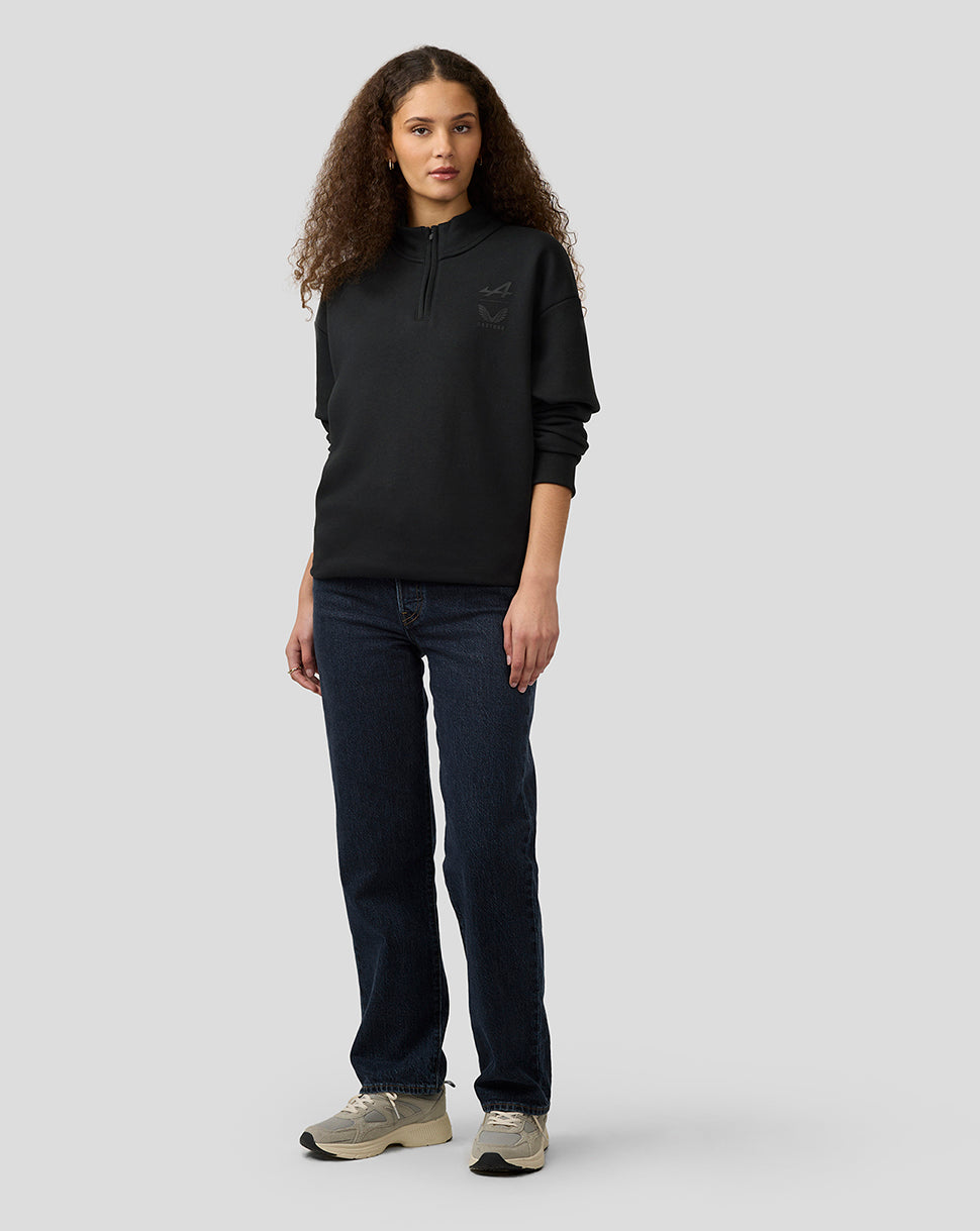 Model wearing black unisex Alpine Castore quarter zip pullover with funnel neckline and relaxed oversized fit chest logos