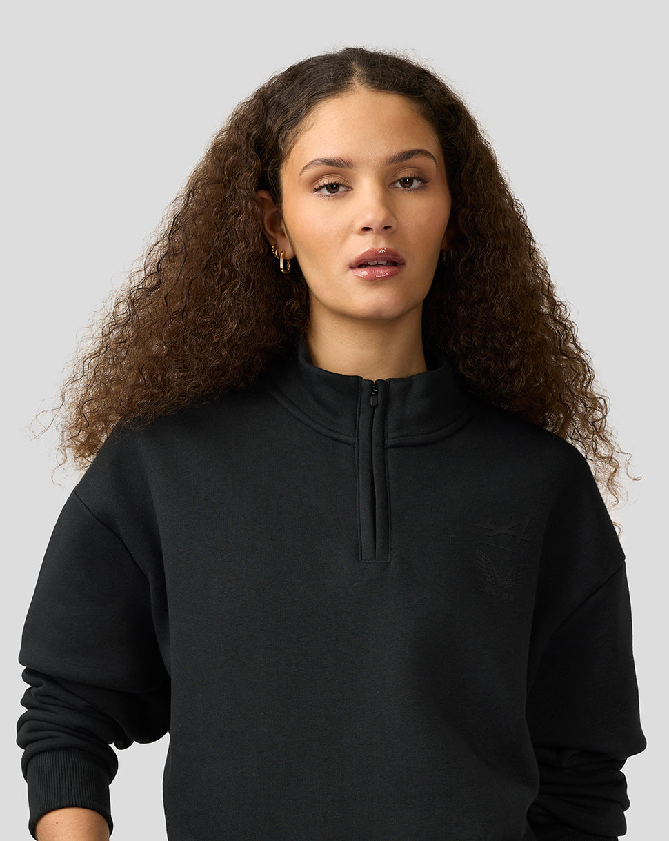 Female model wearing a black Alpine Castore unisex quarter zip pullover with funnel neckline and subtle chest branding.