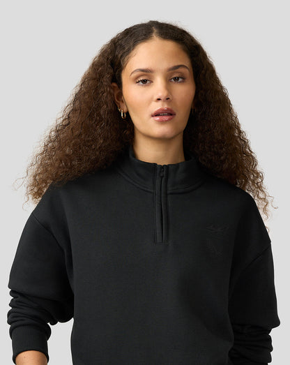 Female model wearing a black Alpine Castore unisex quarter zip pullover with funnel neckline and subtle chest branding.