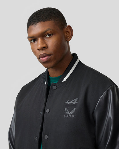 Male model in a black Alpine bomber with leather sleeves and varsity striped cuffs.