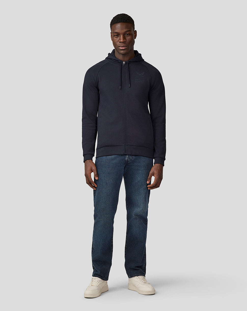 Full body front view of a man in a night sky navy hoodie with hood, chest logo, blue jeans and beige sneakers.