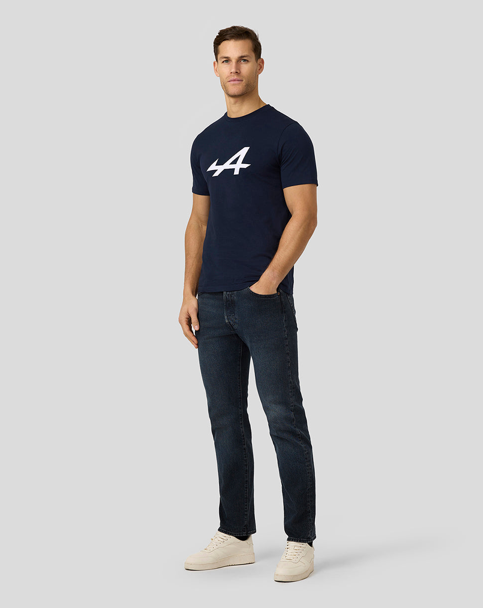 Male model in navy Alpine Core Essentials T-shirt with a large white logo, paired with dark jeans and light sneakers.
