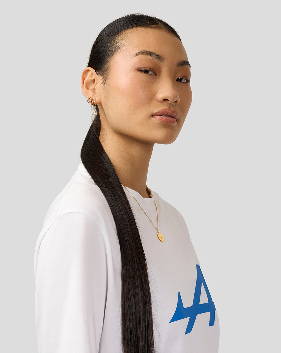 Female model in a brilliant white Alpine Core Essentials T-Shirt with a blue chest logo in a side profile.