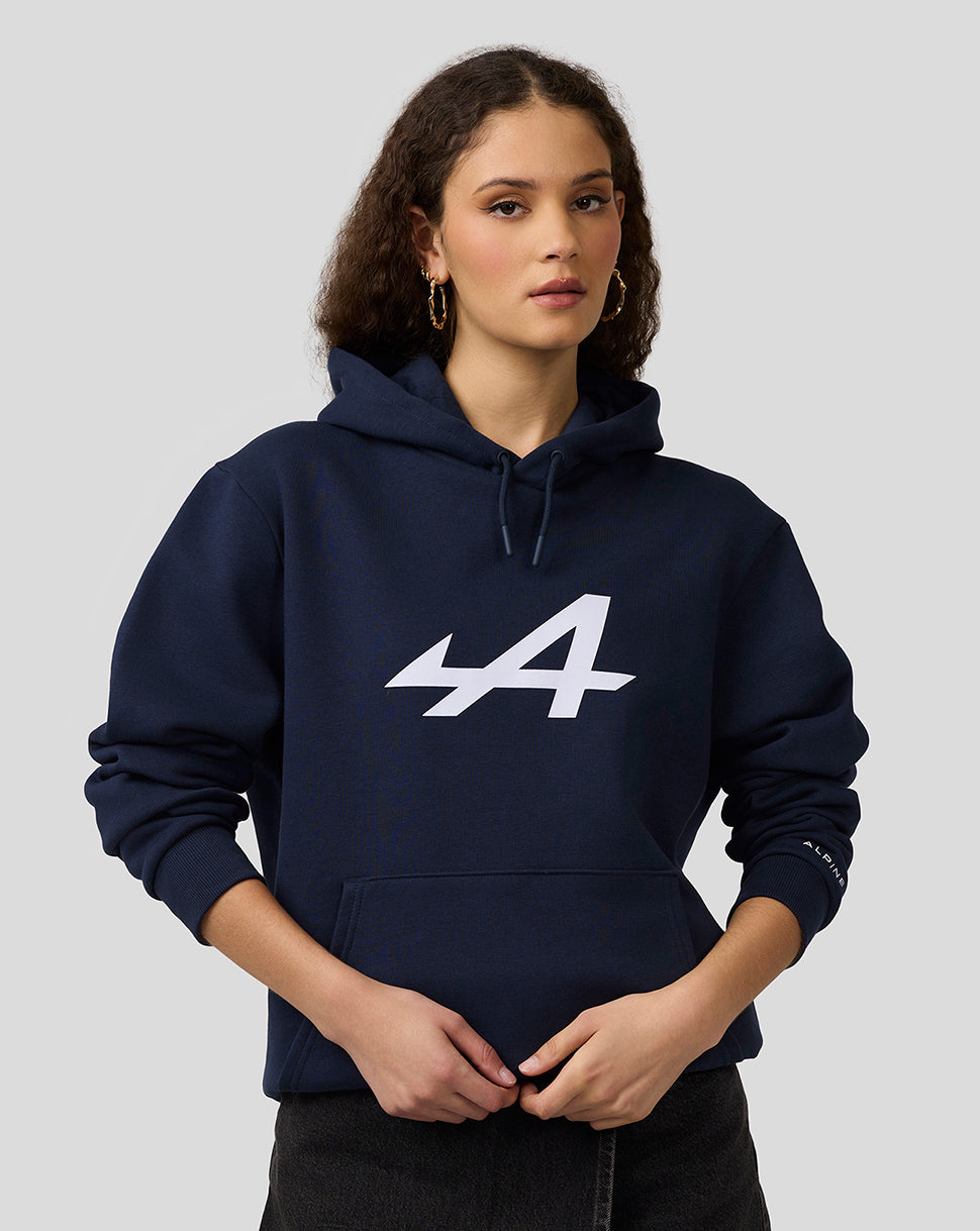 Female model wearing navy Alpine Core Essentials Hoodie with a large center logo and left sleeve logo.