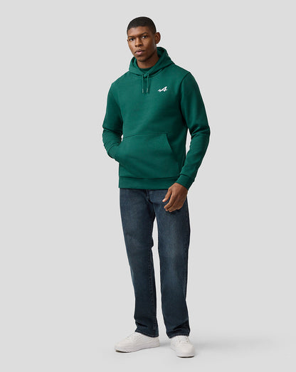 Male model in botanical green Alpine hoodie with front pocket and drawstring hood, paired with jeans and white sneakers.