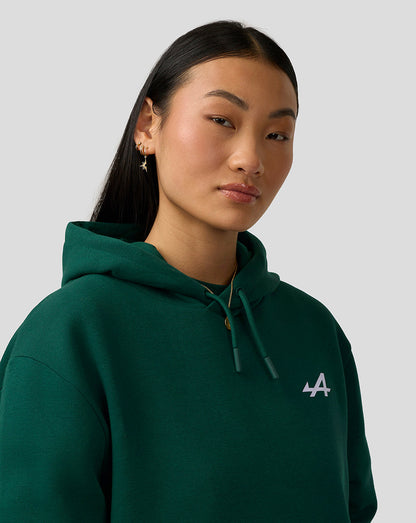 Close-up of female model wearing botanical green Alpine hoodie with white chest logo and drawstring hood