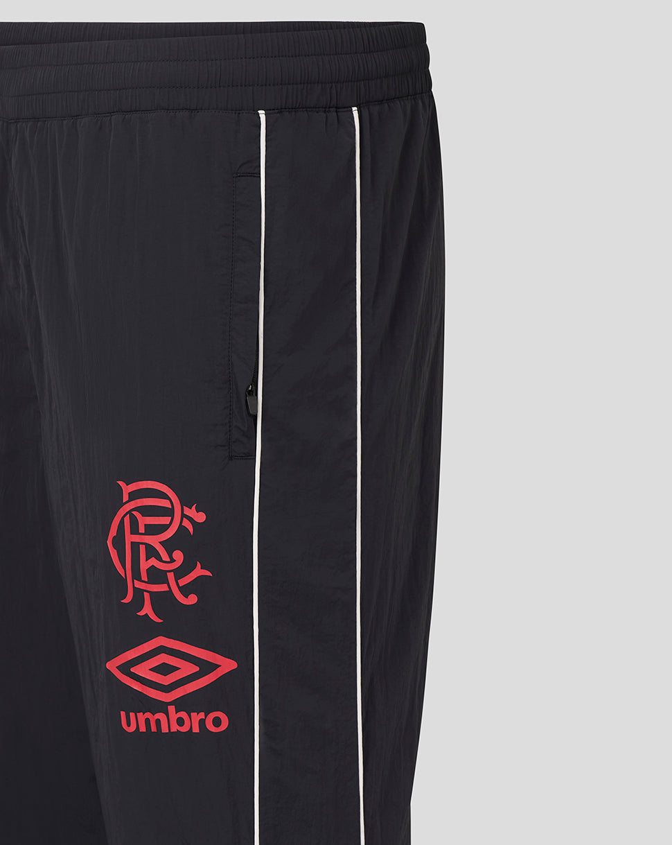 Close-up of the pant leg showing white piping and red crest with Umbro logo on dark fabric