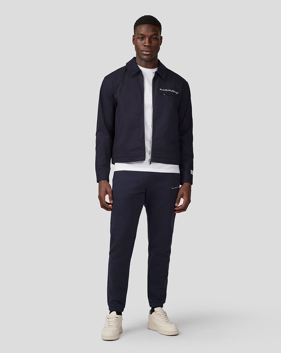Full body shot of a male model in navy night sky cropped script work jacket with white tee and matching navy pants.