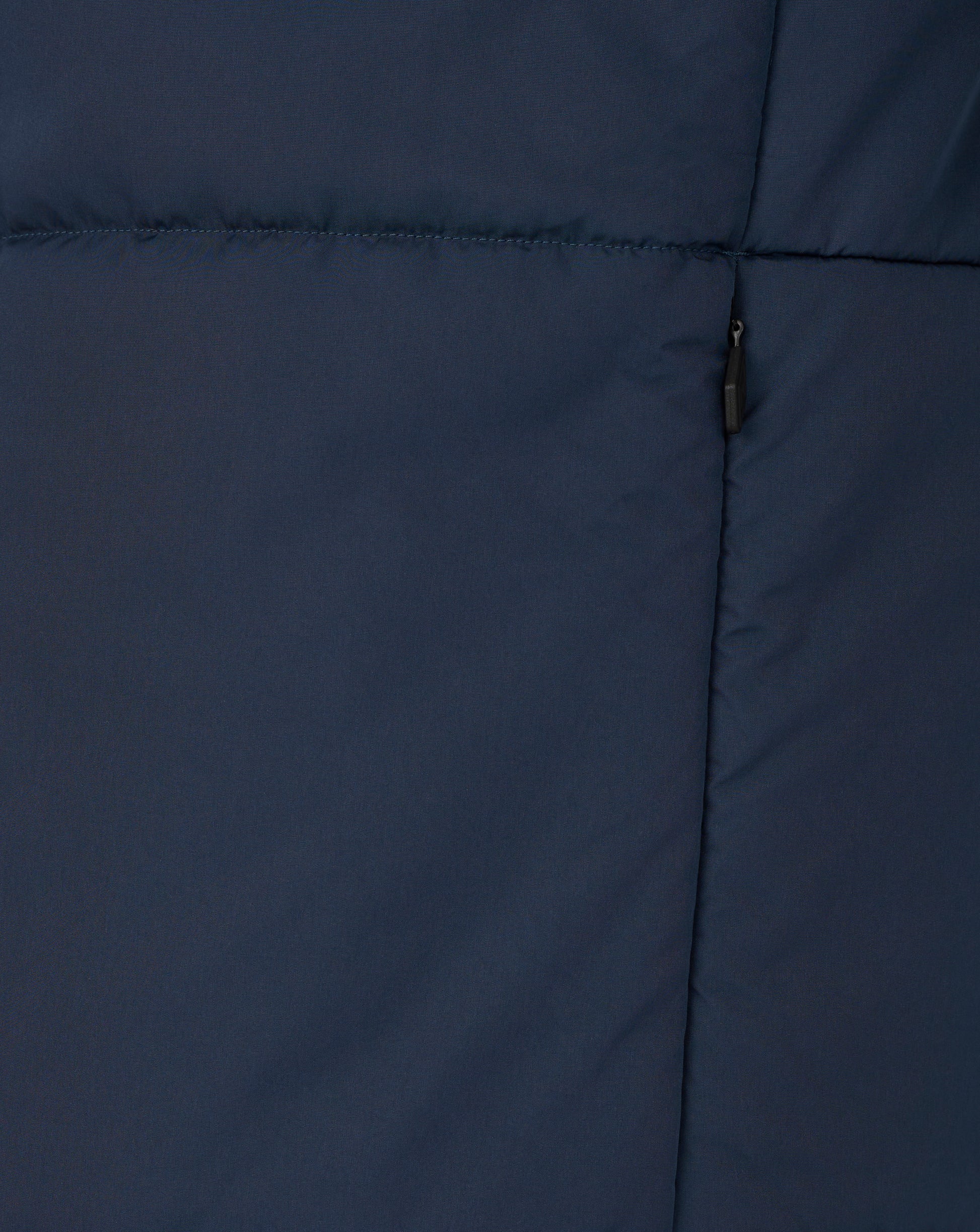 Close up of navy padded training jacket fabric with horizontal stitching and a black zipper pull