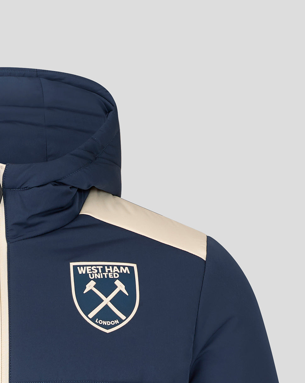 Close-up of West Ham crest on navy padded jacket with cream shoulder panel near the collar.