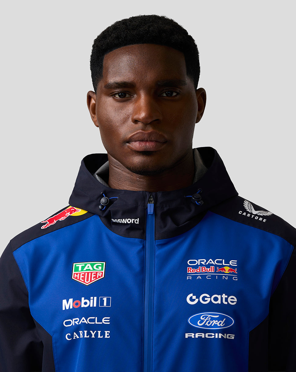 Male model wearing blue and navy Teamline jacket with hood showing multiple sponsor logos on chest and shoulders.