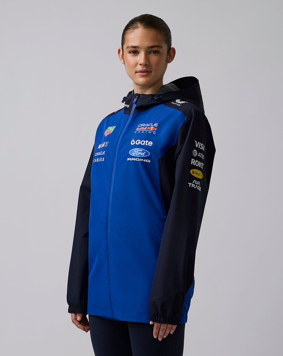 Female model wearing blue and navy Oracle Red Bull Racing Teamline water resistant jacket with hood and chest branding.