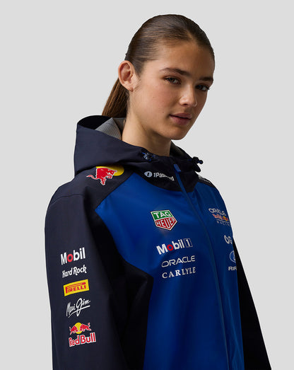 Close up of a model in blue and navy Teamline jacket with hood displaying chest and shoulder sponsor logos.