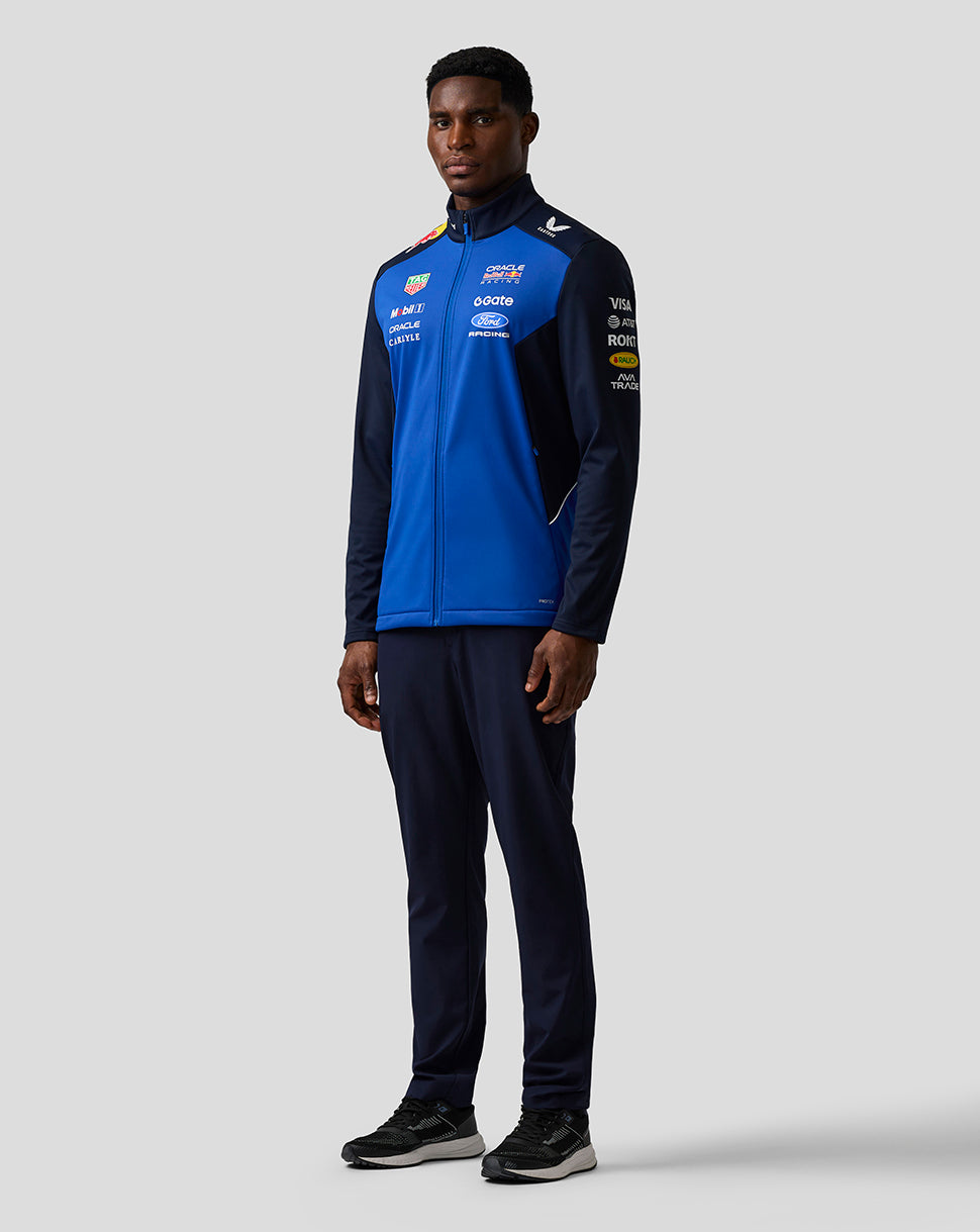 Full length view of a male model in navy night sky Oracle Red Bull Racing Teamline Soft Shell Jacket with front zipper and sponsor logos.