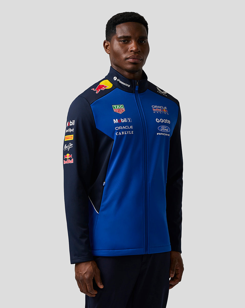Male model wearing blue Oracle Red Bull Racing Teamline Soft Shell Jacket with multiple sponsor logos on chest and sleeve