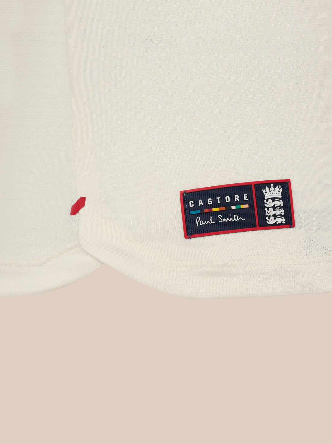 Hem detail of white knit T shirt with a Castore Paul Smith patch and crest on the lower front