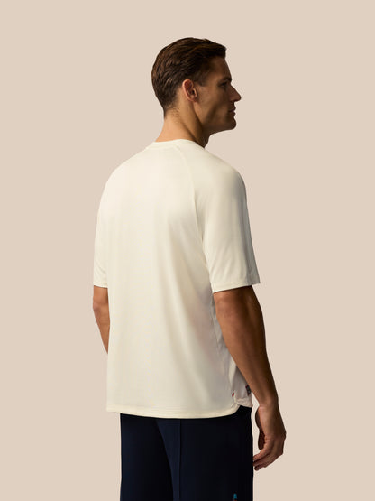 Profile view of a man wearing a cream knit T shirt against a beige background